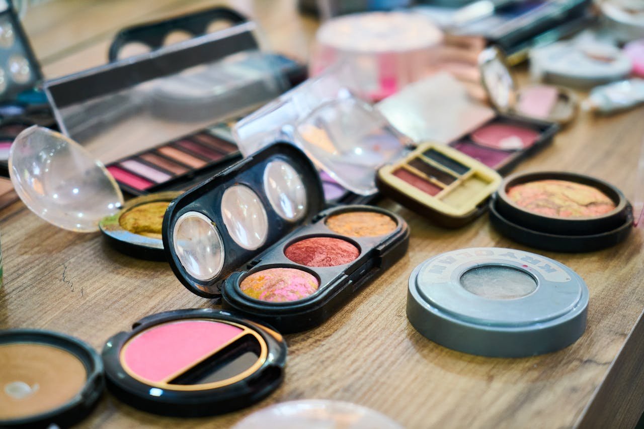 A variety of colorful makeup palettes and cosmetics organized on a wooden table.